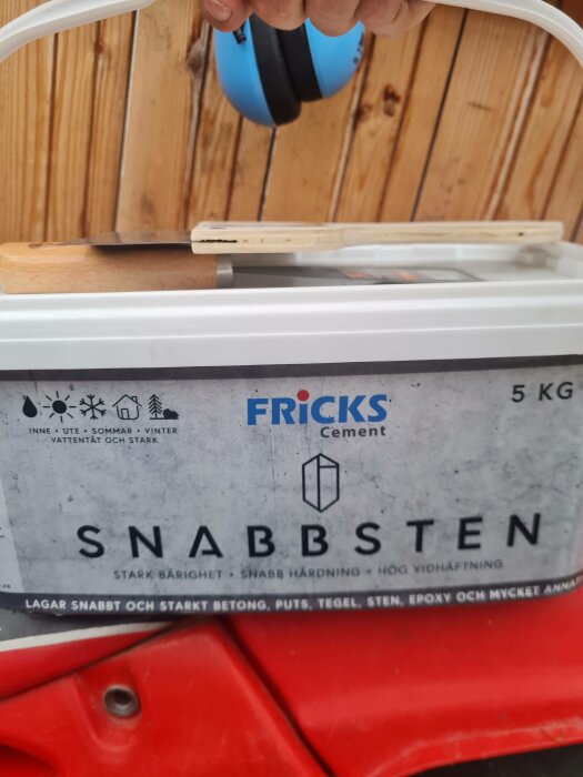 Säck med SNABBSTEN från FRICKS Cement, troligtvis på en byggplats, med någons hand i blå handske.