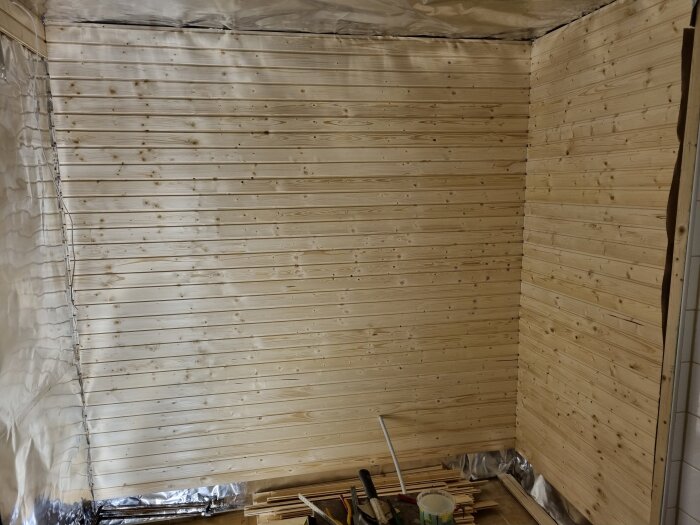 Träpaneler på väggar i rum under konstruktion, byggmaterial och verktyg på golvet.