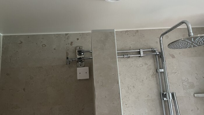 Modernt badrum, kakelvägg, duschhuvud, rör, termostat, väggmonterad ljusknapp, del av tak.