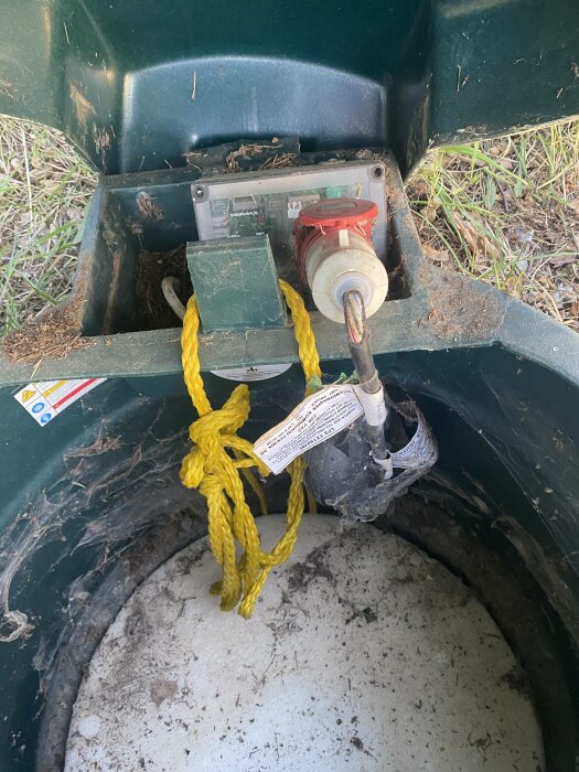 Vinsch med gul rep och varningsetikett i brunnen, elektrisk komponent och skräp.