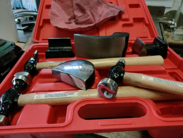 Röd verktygslåda innehåller olika hammare, verkstadsbakgrund, arbetsbänk, handverktyg, metallblänk.