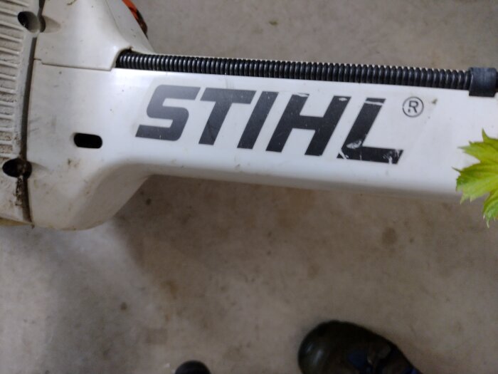 Del av en STIHL-maskin, sannolikt trädgårdsutrustning, med märkeslogotyp synlig och lite smutsig.