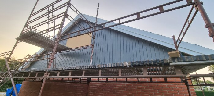 Byggnad under konstruktion med ställningar, blåa väggar, tegel och träbjälkar. Skymning eller gryning i bakgrunden.