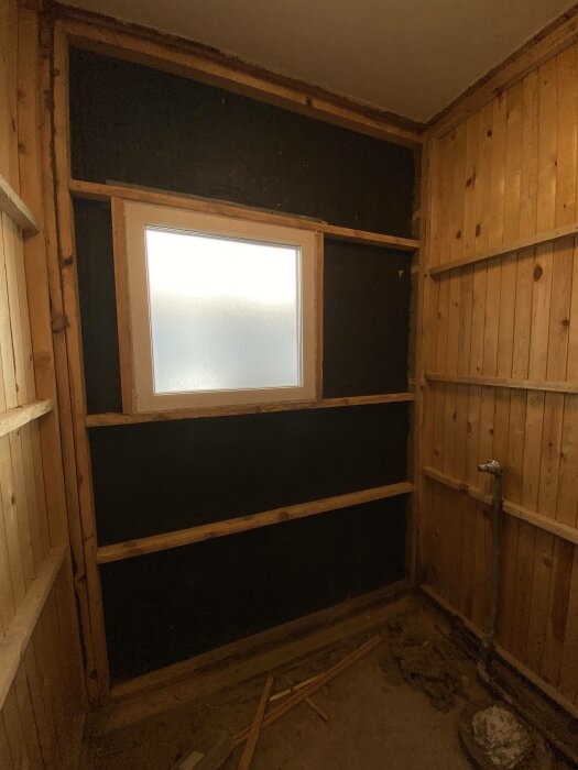 Ett ruffigt rum under renovering med träväggar och ett fönster som släpper in ljus.