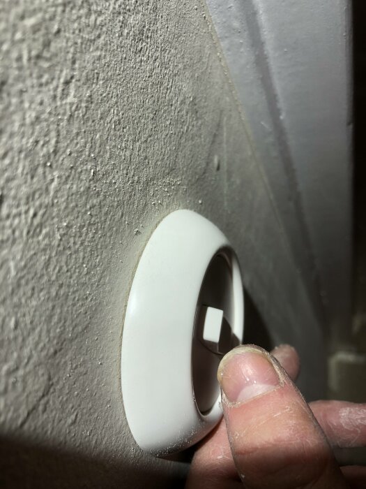 En hand justerar en vit, rund termostat på en texturerad vägg. Rumsdetalj, närbild.