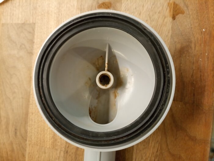 Översikt av en använd mixerbehållare med skärblad, fläckar, på ett träunderlag.