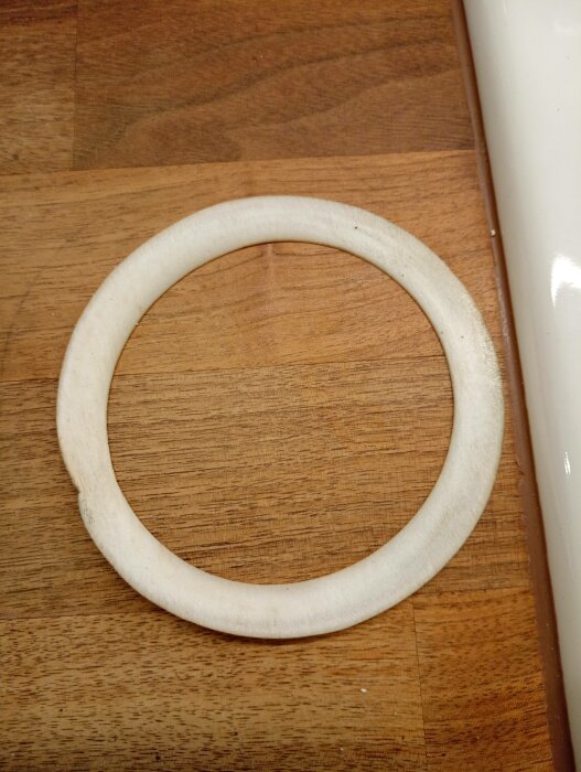 Rund, vit silikon eller gummi-tätning på träbakgrund nära en vit kant.