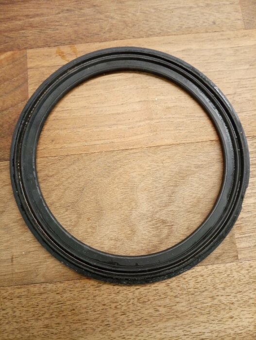 Svart gummipackning på träyta. Rund form, tätningselement, teknisk komponent.