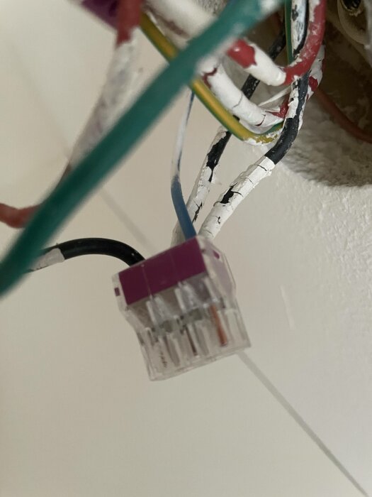 Ett nätverkskabelhuvud, en RJ45-kontakt, kopplad till skadade kablar; potentiellt osäker elektrisk installation.