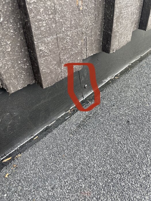 Trästaket vid asfaltväg, röd markering kring svart skada eller öppning. Närbild, detaljorienterad, utomhus.