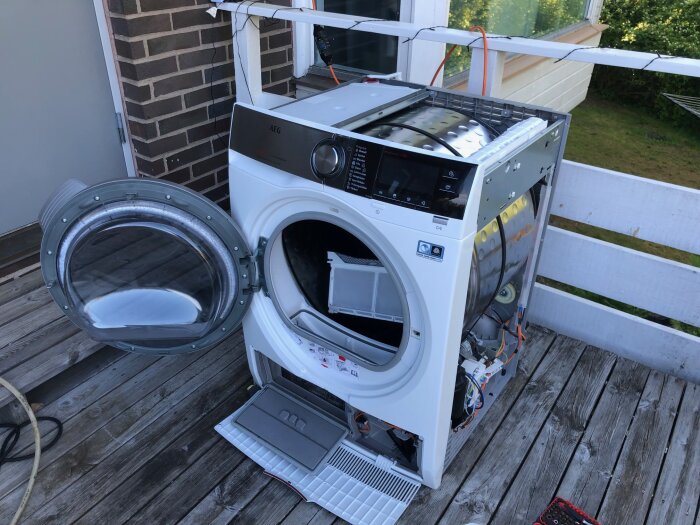 Trasig eller demonterad tvättmaskin på en trätrall utomhus.
