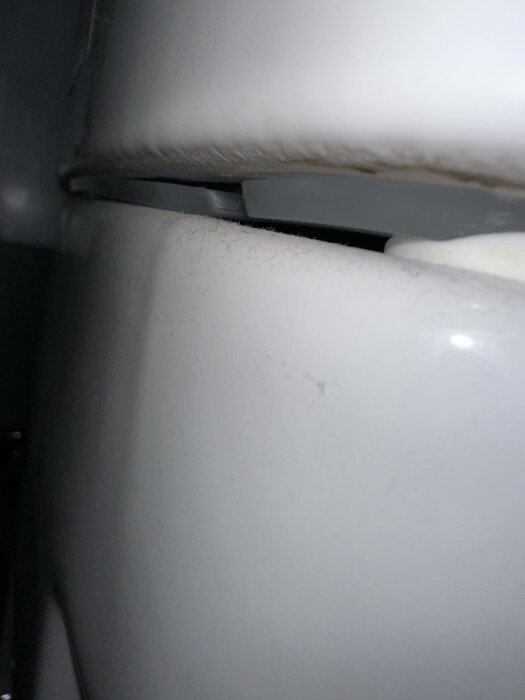 Närbild av vit strukturerad yta med skugga och oskarpa konturer, sannolikt del av en möbel eller apparat.