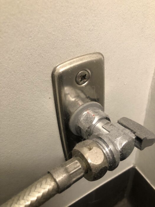 Metallventil och röranslutning på vägg. Sanitär installation, stängd vinkelventil, gråa nyanser, skruv, stålrör.