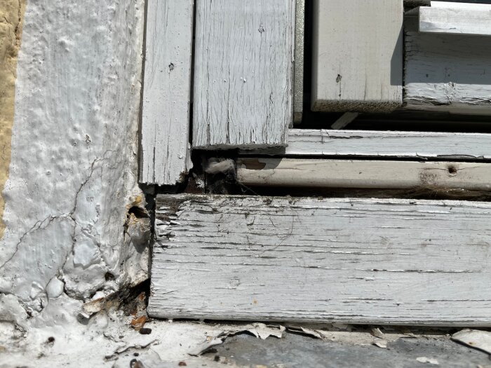 Slitna träytterpaneler och fönsterkarmar med flagande färg vid ett hus.