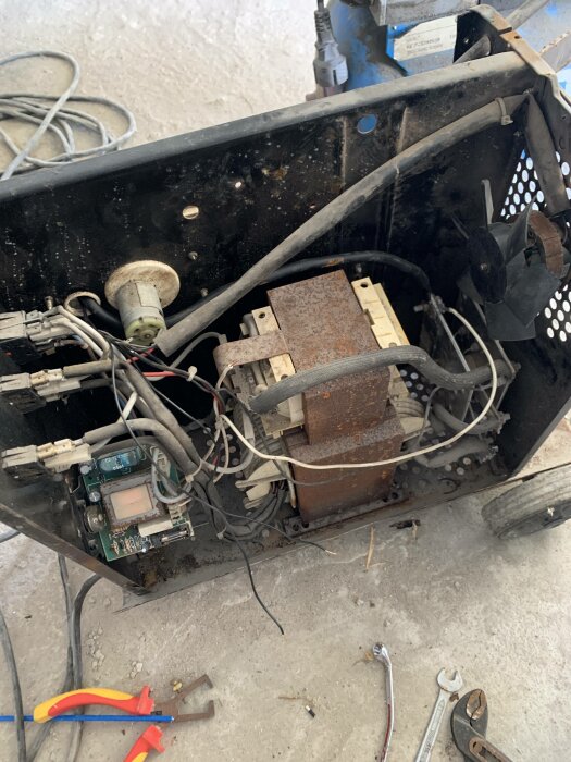Nermonterad elektrisk apparat, rost, kablar, kretskort, verktyg på smutsigt betonggolv. Reparation eller skrotning.