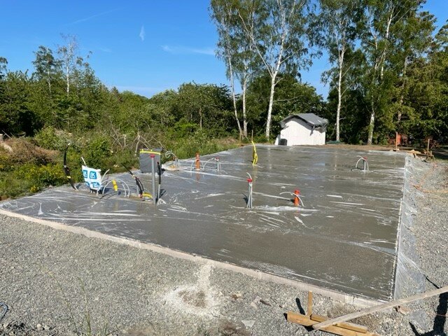 Nyutgjuten betongplatta med avspärrningsband, inbyggda installationer, i dagsljus, omgiven av natur och en byggnad.