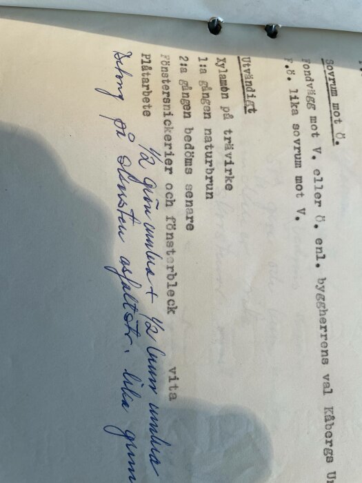 Sidans del med text, handskrivna anteckningar på svenska, skugga av en hand, lutande bild.