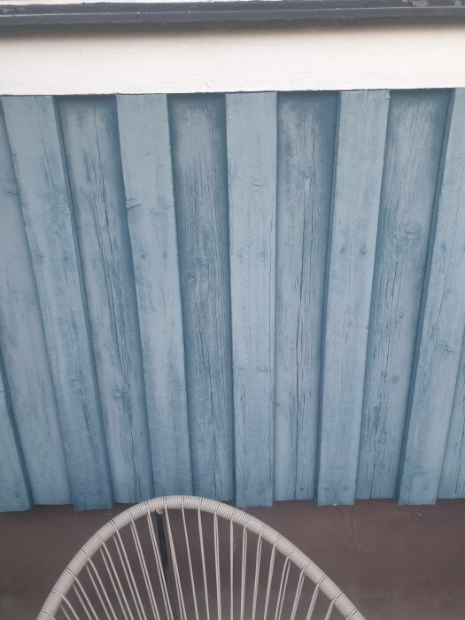 Blå trävägg, del av vit stol framför, enkel arkitektonisk detalj, utomhusbelysning, dagsljus.