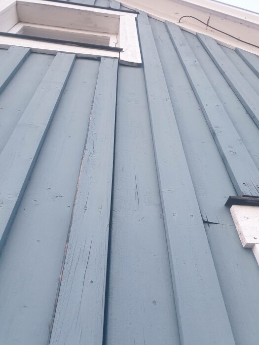 Blå träfasad, vit fönsterkarm, vertikala paneler, arkitektonisk detalj, byggnadsexteriör, lutande perspektiv.