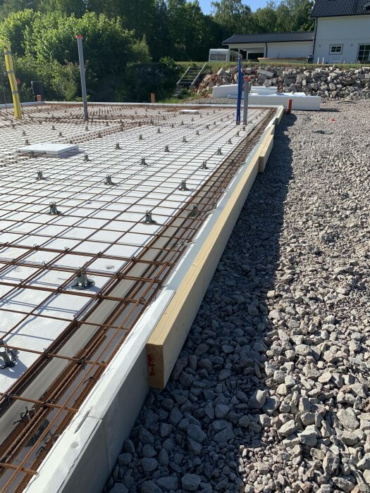 Byggarbetsplats med armeringsjärn, gjutformar, grus och tillbehör för betonggjutning under solig himmel.