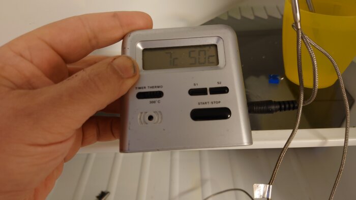 Hand håller digital termometer med timer, visar 50 grader Celsius, köksmiljö, matlagningsverktyg.