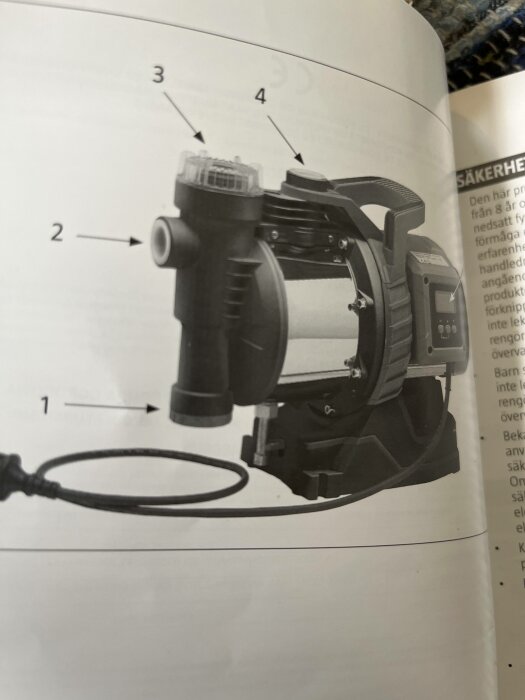 Svartvit bild av elektrisk maskin med numrerade komponenter, instruktionsmanual med säkerhetsinformation, kablar, delvis suddig.