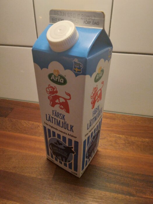 Ett paket Arla färsk lättmjölk på träyta, blått och vitt med datumstämpel, en liter.