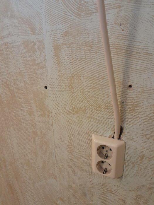 Dubbel eluttag på trävägg, med kabel ansluten, spår av spikar, oavslutad eller rustik stil.