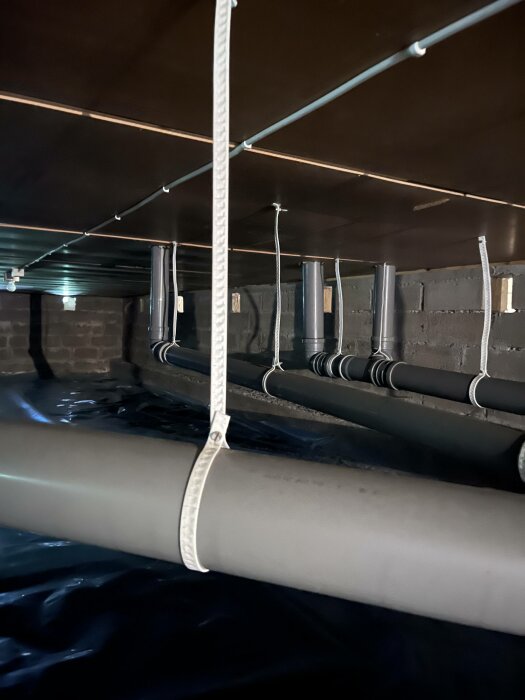 Rör och kablar under golv, säkrade med spännband, mörka färger, dolt utrymme, infrastruktur.