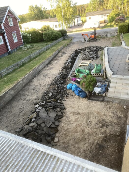 Trädgård under anläggning, stenläggning, grävmaskin, stenmur, hus, grönska, trädgårdsarbete, vår eller sommar, soligt väder.