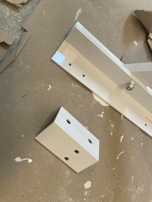 Metallstycke och block, antagligen möbeldelar, på ett dammigt betonggolv under konstruktion eller renovering.