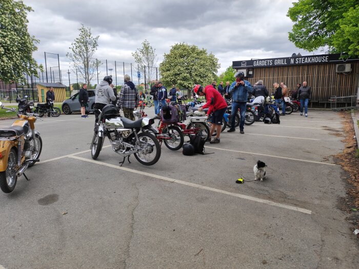 Motorcykelträff med människor och en hund, utomhus vid en grill och steakhouse-restaurang, molnig himmel.