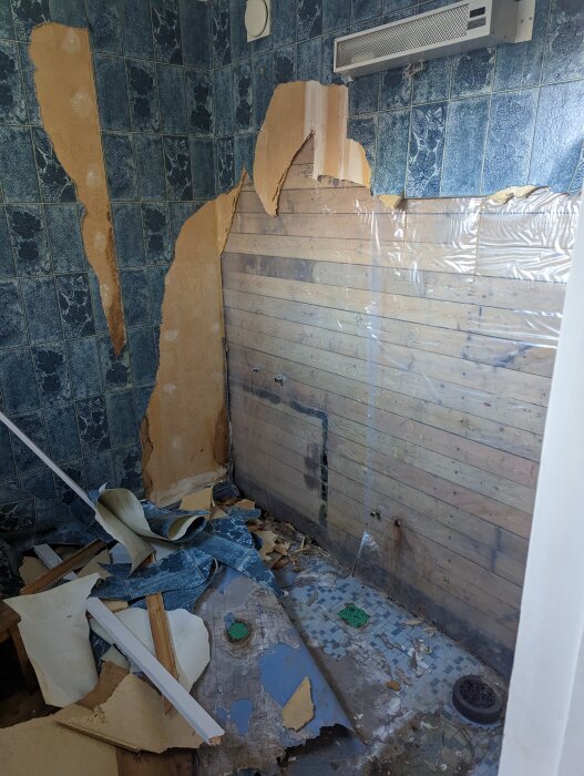 Renoveringsarbete i badrum med rivna väggar, skräp, gammal kakel och träbjälkar synliga. Nedrivet och ostädat.
