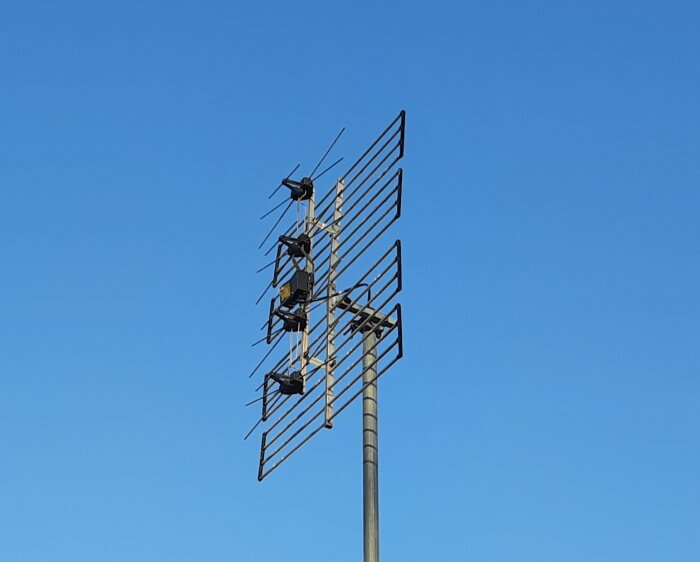 TV-antenner monterade på mast mot klarblå himmel.