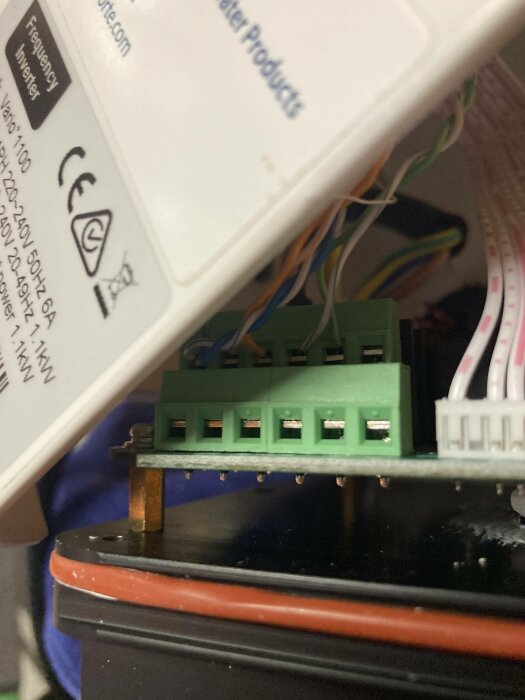 Elektronisk enhet med grön klemrad, kablar och vit etikett med CE-märkning synlig.