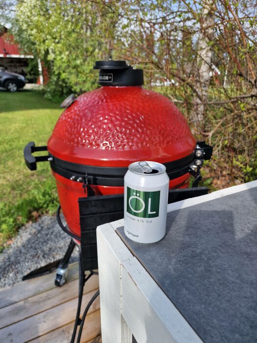 Röd grill, ölburk på bord, trädgård bakgrund, soligt.