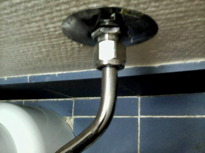 Väggmonterad anordning för vattenförsörjning, flexibel slang, flisplattor, toalett synlig, installationsdetaljer.