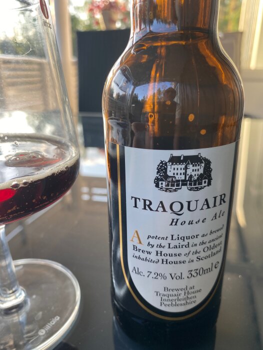 Ölflaska märkt "Traquair House Ale", glas med mörk öl, reflektion av en person, inomhusmiljö, dagsljus.