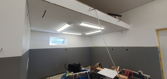 Renoveringsrum med öppet tak, byggmaterial, verktyg och LED-belysning.