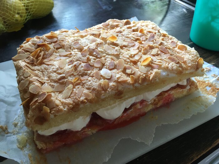 Ett lager av tårta med grädde och sylt, toppad med rostade mandelspån, på ett köksbord.