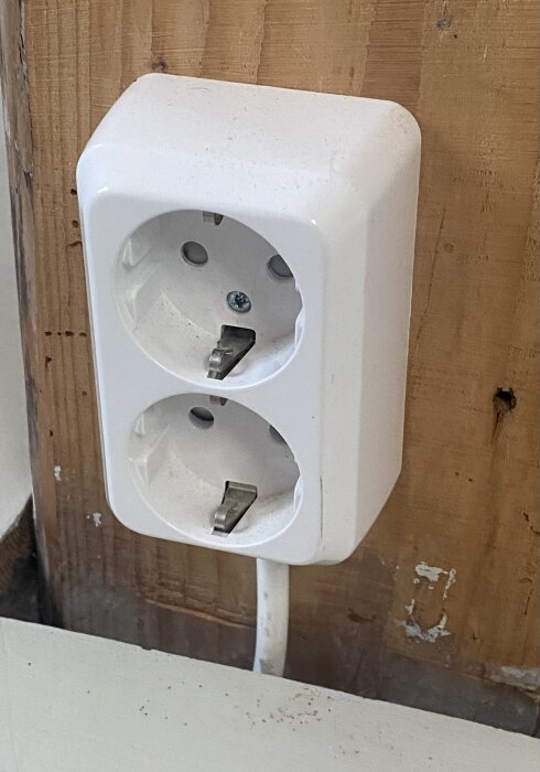 Dubbel eluttag monterat på en vägg, med synliga träreglar och en ansluten kabel.