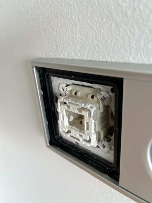 Öppen väggströmbrytare utan knapp, exponerad installation, grå ram på vit vägg.