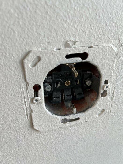 Öppen elektrisk vägguttag utan skyddande täckplatta, exponerade anslutningar och trådar, installationsarbete pågår.