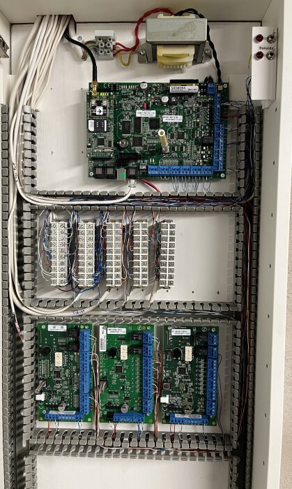 Öppen elektrisk styrpanel med kretsar, kablar och reläterminaler inom industri eller byggnadsteknik.