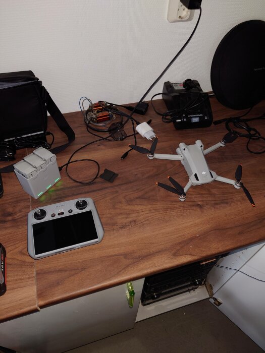 Arbetsyta med drönare, kontroller, laddare och elektronisk utrustning. Oordnat med sladdar och teknikprylar.