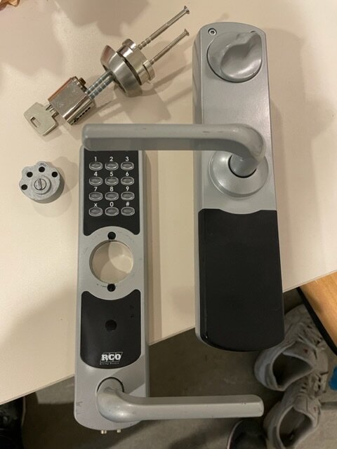 Isärr och elektronisk dörrhandtag med kodlås och nyckelcylinder, demonterade delar, säkerhetsteknik, grå bakgrund.