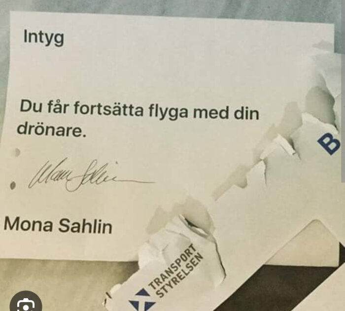 Delvis riven handling med text "Intyg... Du får fortsätta flyga med din drönare" och namnteckning, på vit bakgrund.