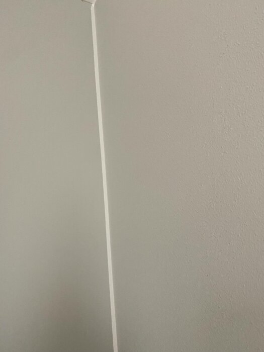 Ljusgrå vägg med ett lodrätt, smalt, framträdande list eller kabel. Enkel, minimalistisk design.