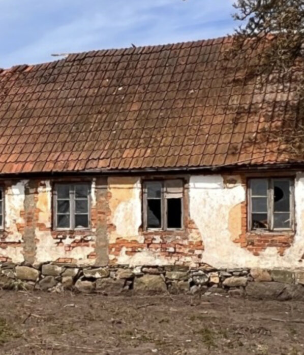 Förfallen lada, tegel, spruckna fönster, avskalad puts, tegeltak, ingen växtlighet, klar himmel, övergivet intryck.