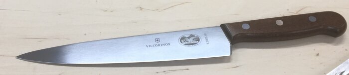 Victorinox kökskniv med trähandtag ligger på ljus träyta.